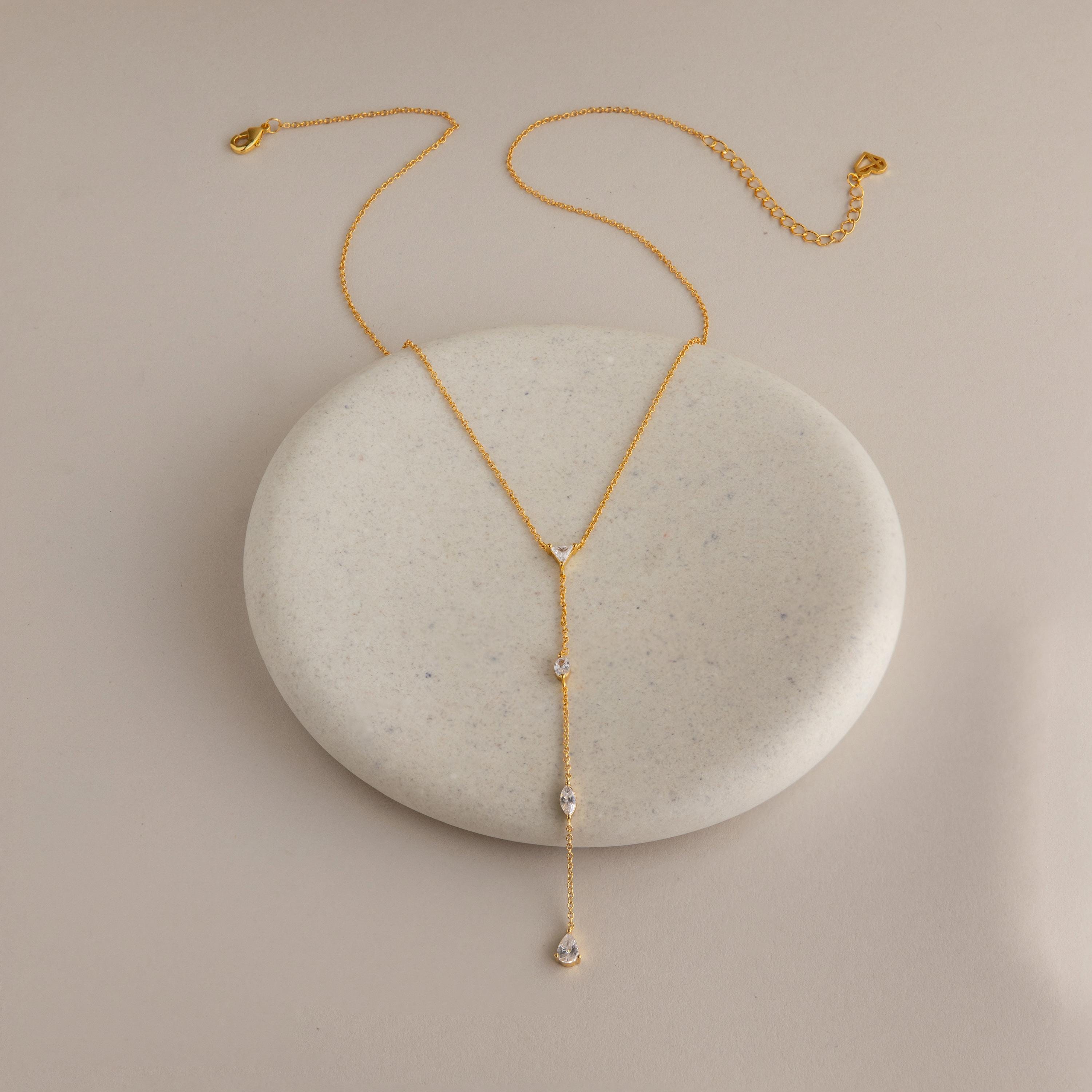 The Mixed Diamond Lariat Necklace features diamond gemstones displayed on a round, light stone with a beige background—an elegant piece perfect for any occasion.