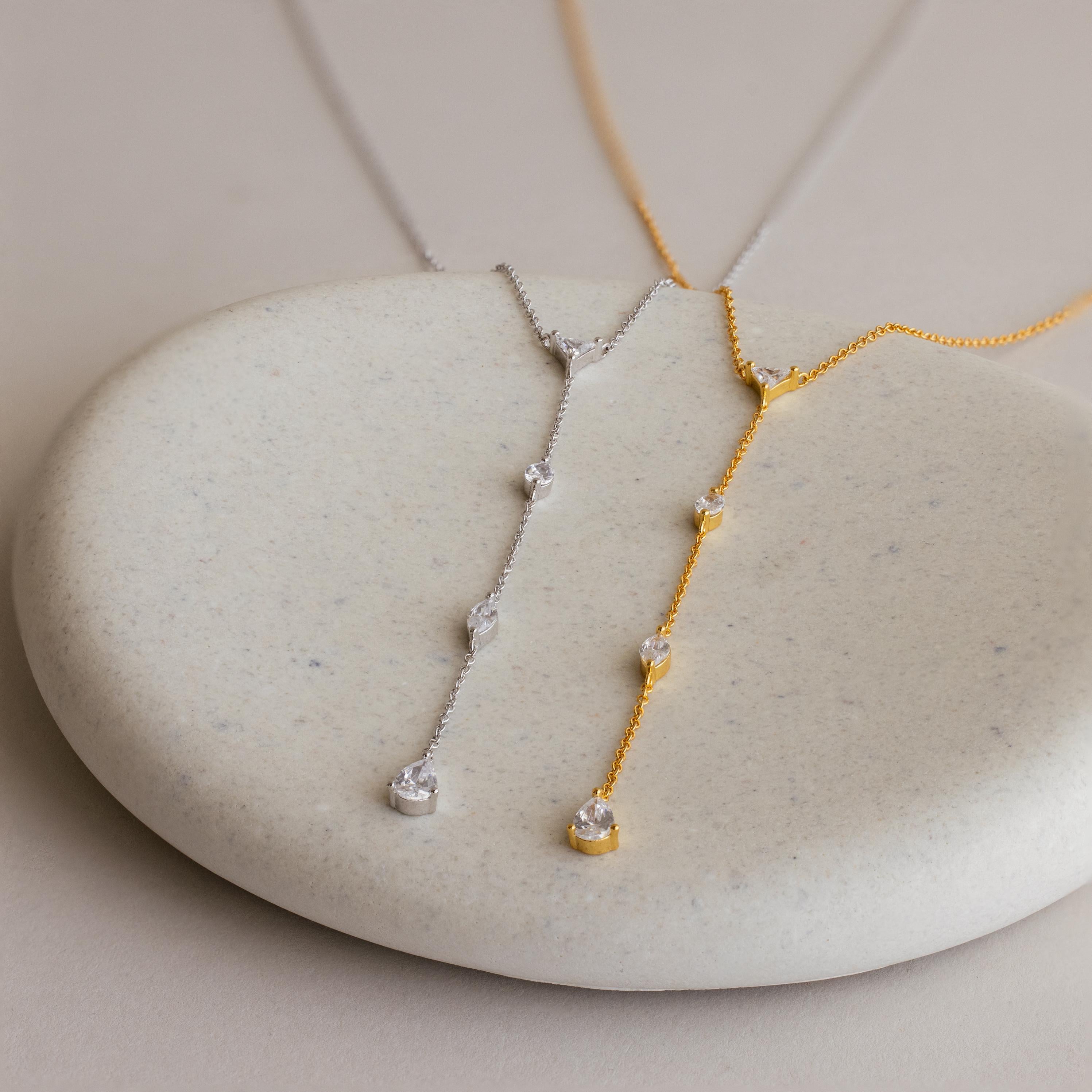 The Mixed Diamond Lariat Necklace, crafted in gold and silver with sparkling diamond gemstones, is elegantly displayed on a smooth stone.