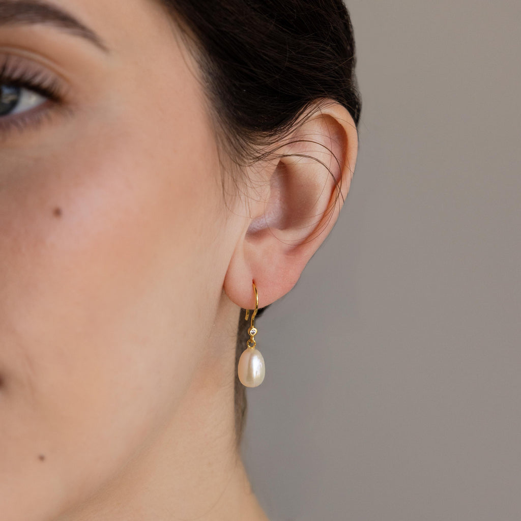Close-up of a woman's ear wearing Dangling Pearl Diamond Earrings featuring elegant gold hoops and a hanging white pearl, highlighting their timeless beauty.