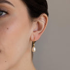 Close-up of a woman's ear wearing Dangling Pearl Diamond Earrings featuring elegant gold hoops and a hanging white pearl, highlighting their timeless beauty.