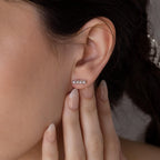 A close-up of a woman’s ear wearing Dainty Pearl Bar Studs—minimalist earrings—with manicured fingers gently touching her ear.