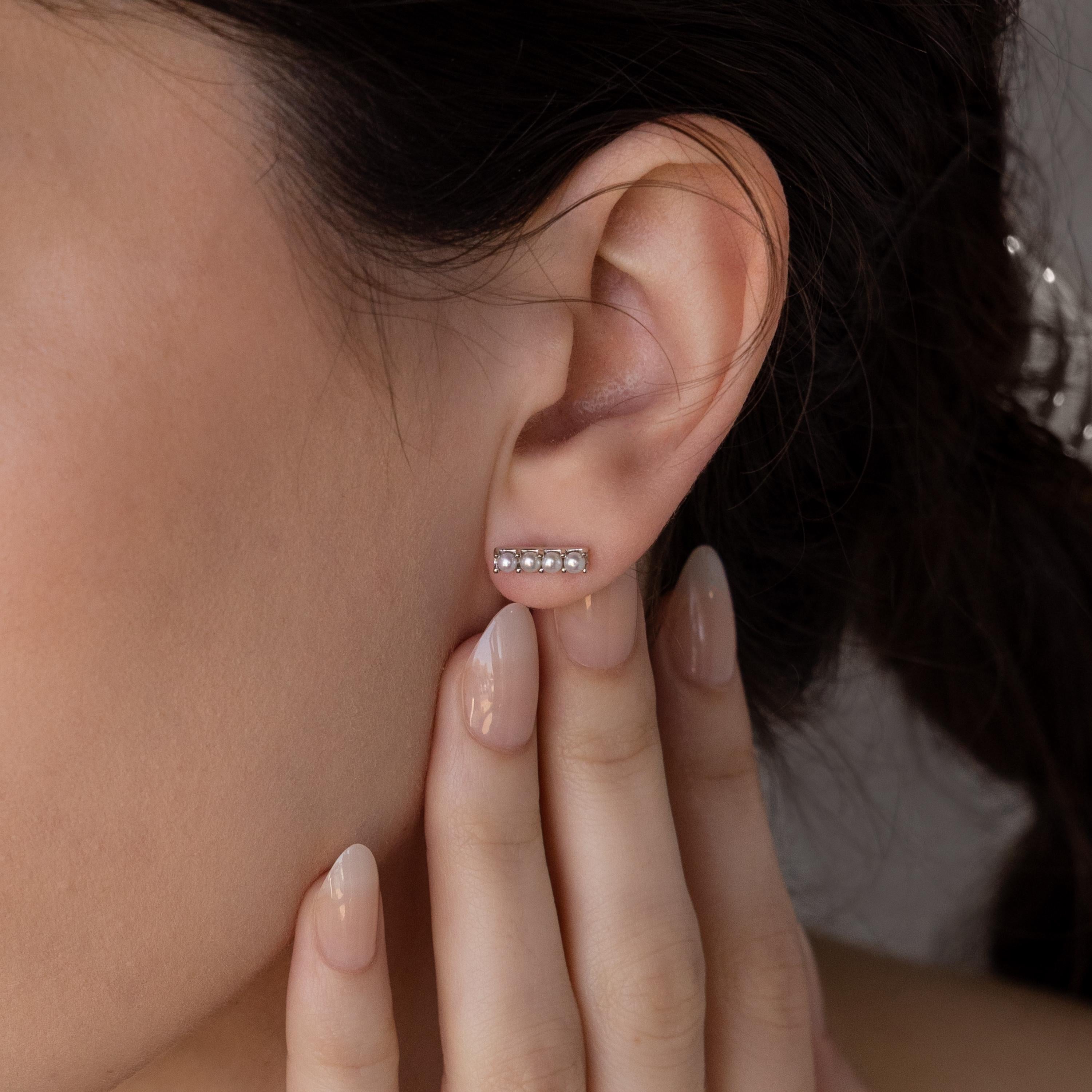 A close-up of a woman’s ear wearing Dainty Pearl Bar Studs—minimalist earrings—with manicured fingers gently touching her ear.