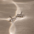 The Dainty Pearl Bar Studs are minimalist silver earrings, each featuring three small pearls in a bar design, displayed on a light textured surface.