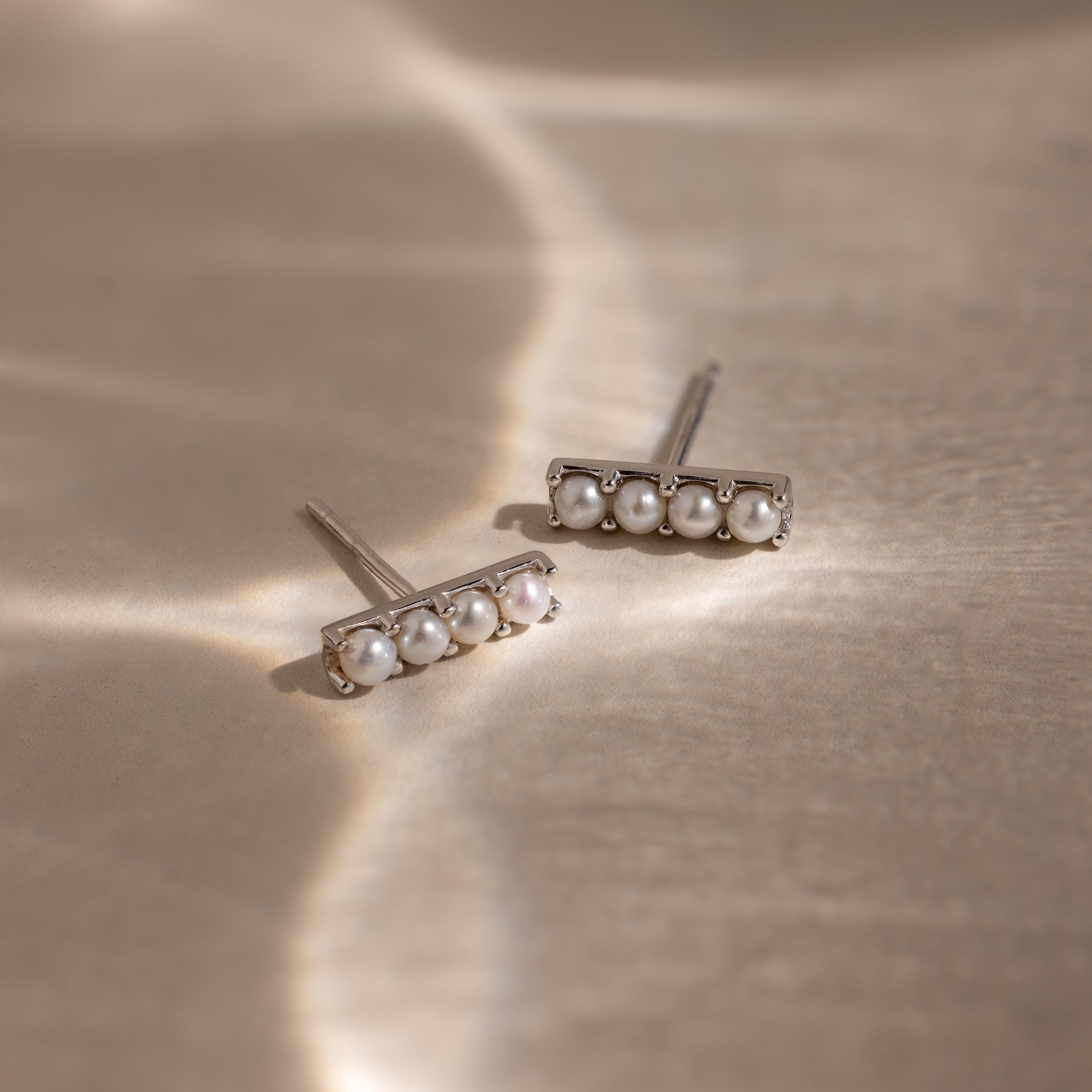 The Dainty Pearl Bar Studs are minimalist silver earrings, each featuring three small pearls in a bar design, displayed on a light textured surface.