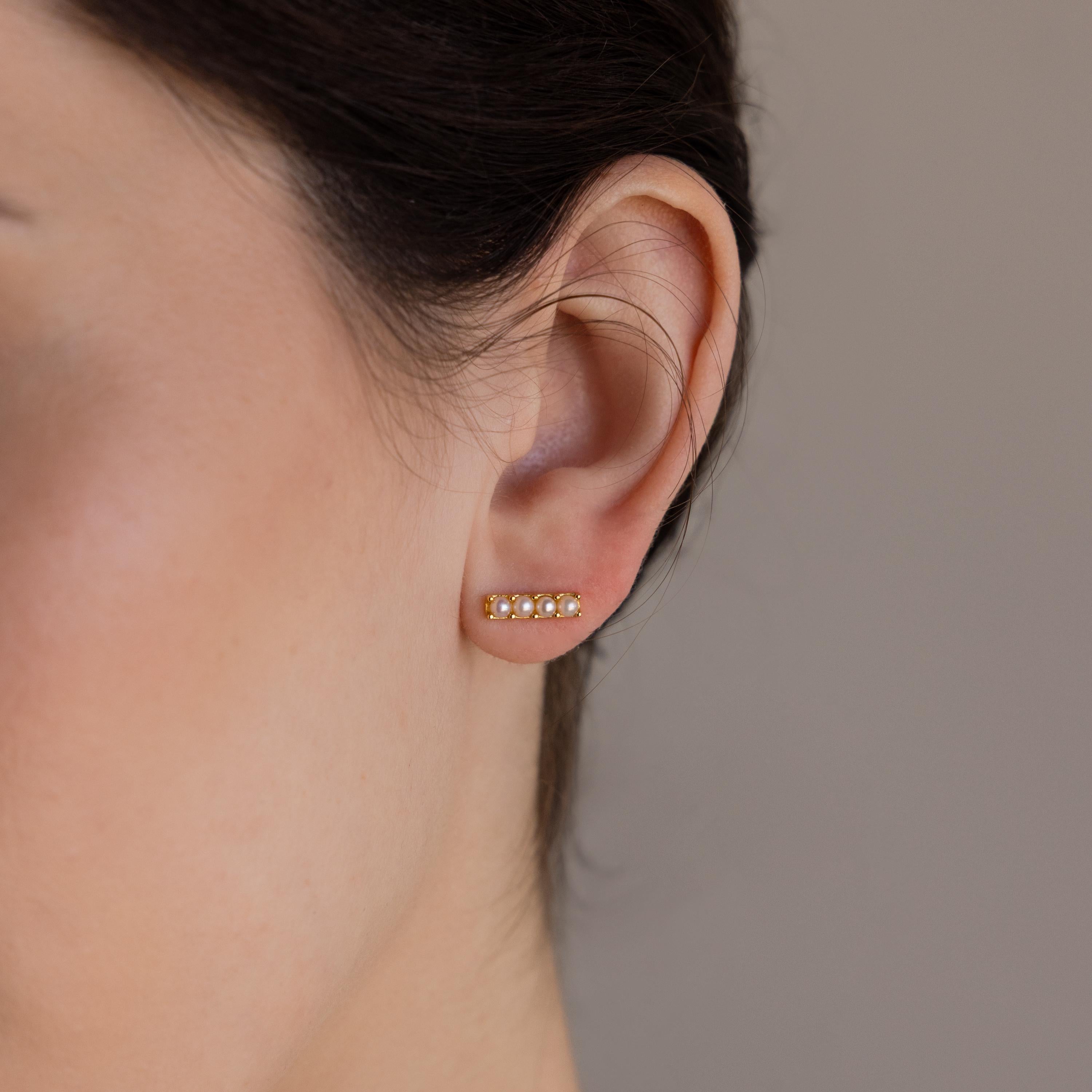 Close-up of a woman's ear wearing Dainty Pearl Bar Studs—minimalist gold earrings featuring small pearls arranged in a row.