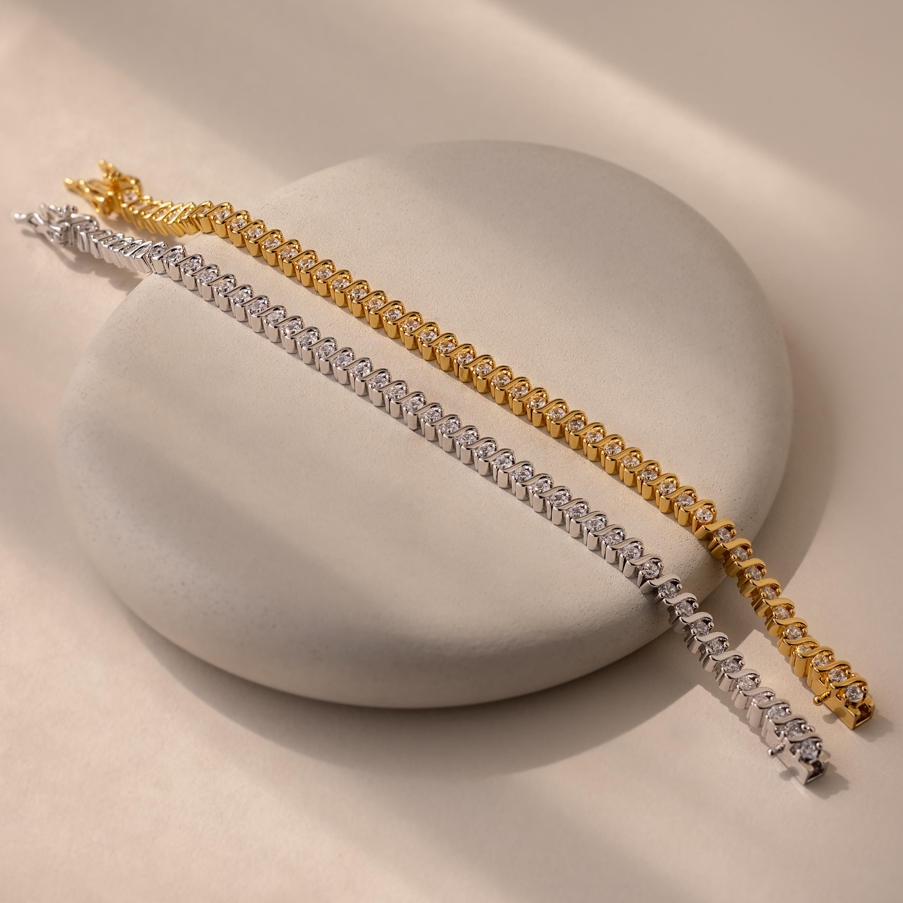 Two elegant chain bracelets, one gold and one silver, displayed on a round beige surface—an ideal pairing with your S-Link Diamond Tennis Bracelet.