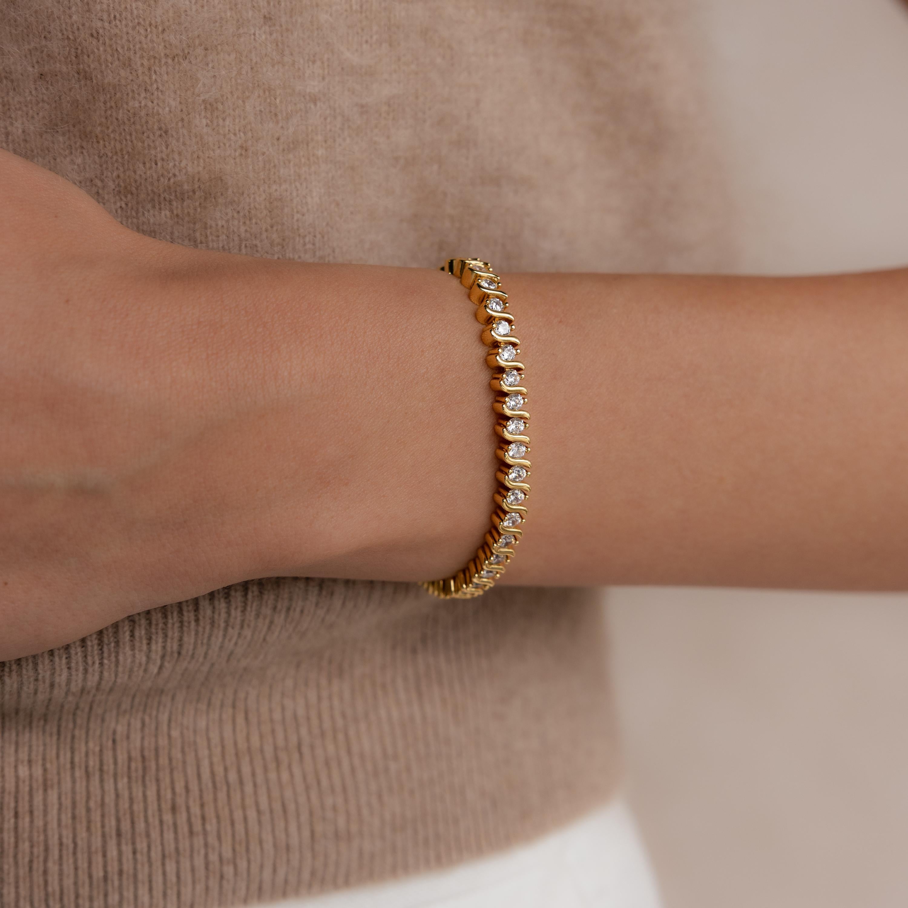 A woman wears the S-Link Diamond Tennis Bracelet, its shimmering stones elegantly paired with a beige sweater.