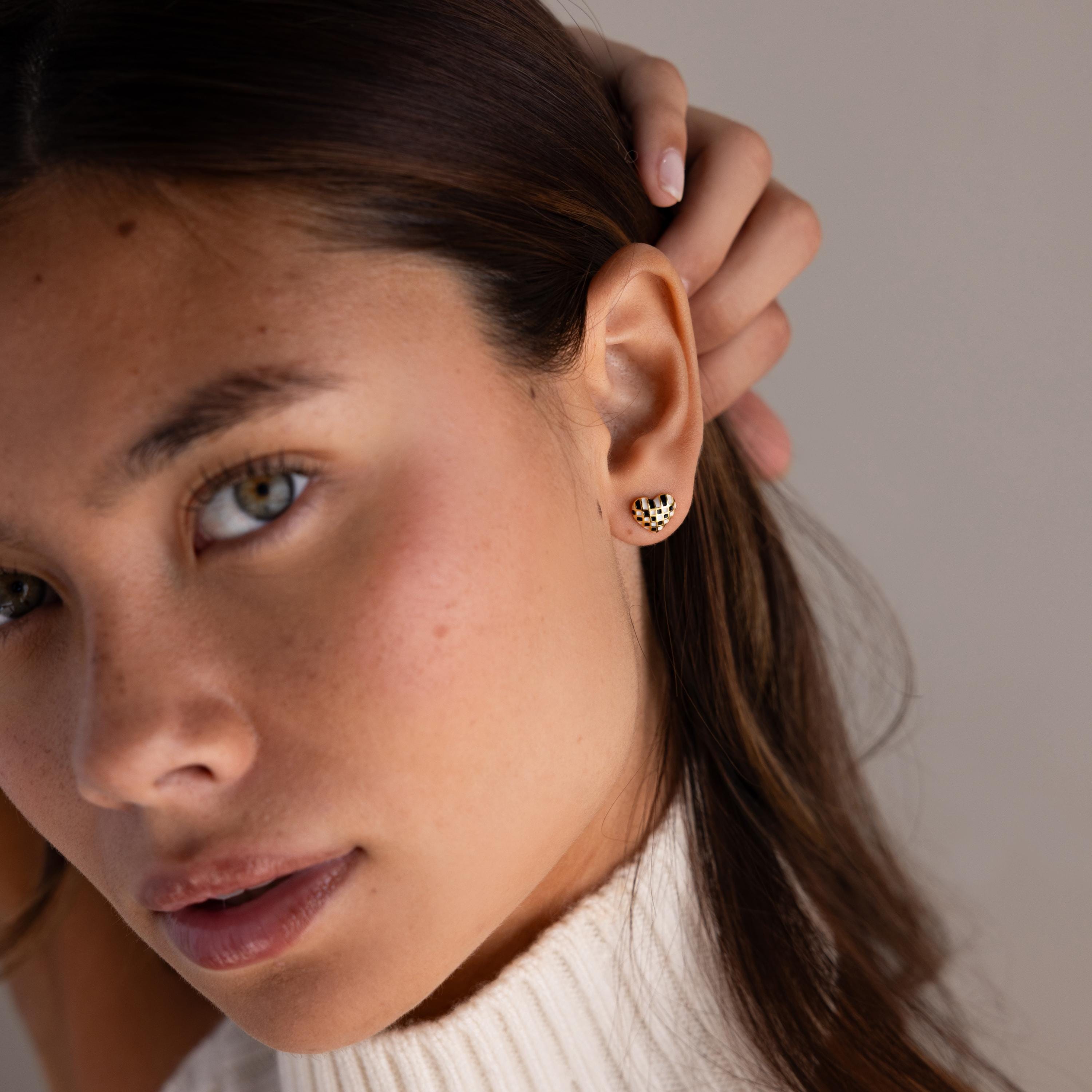 A woman with long hair wears a white sweater and Checkered Heart Studs.
