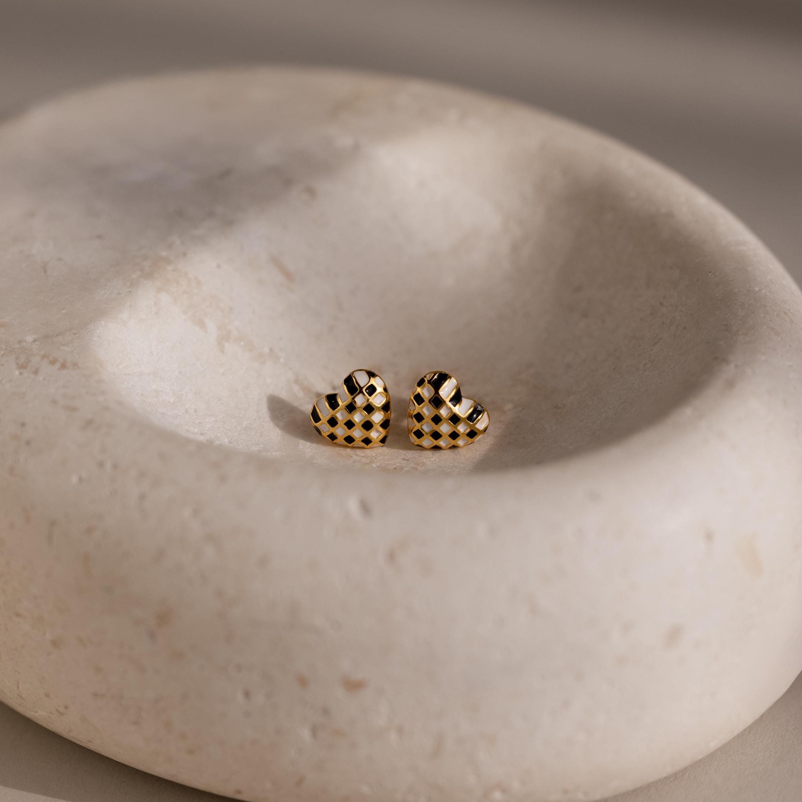 Checkered Heart Studs feature a retro black checkered pattern with a gold finish, beautifully displayed in a smooth, shallow stone dish.