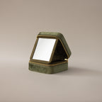 The Velvet Mirror Jewelry Box in green features a square velvet design with a zipper and opens to reveal a mirror—ideal as a compact travel jewelry box, displayed on a plain background.