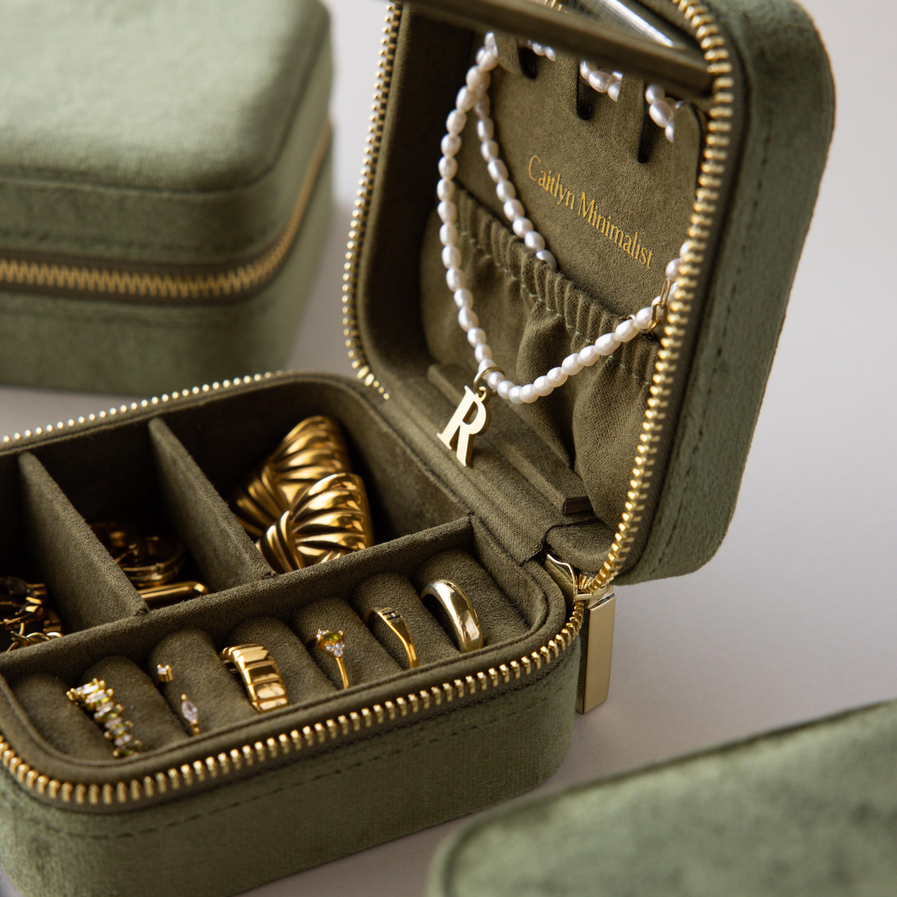 The Velvet Mirror Jewelry Box holds gold rings, hoop earrings, and a pearl necklace with an R pendant—ideal for keeping your favorite pieces organized and stylish.