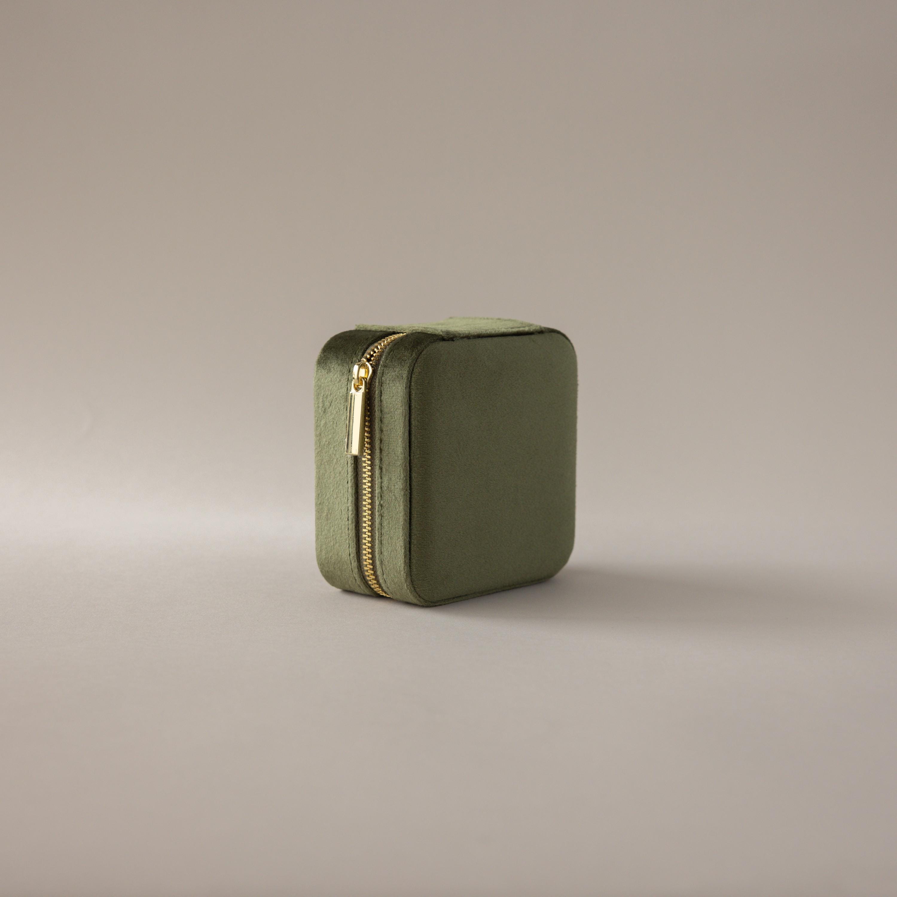 The Velvet Mirror Jewelry Box in olive green features a square velvet design with a gold zipper, ideal as a travel jewelry box, shown on a neutral background.