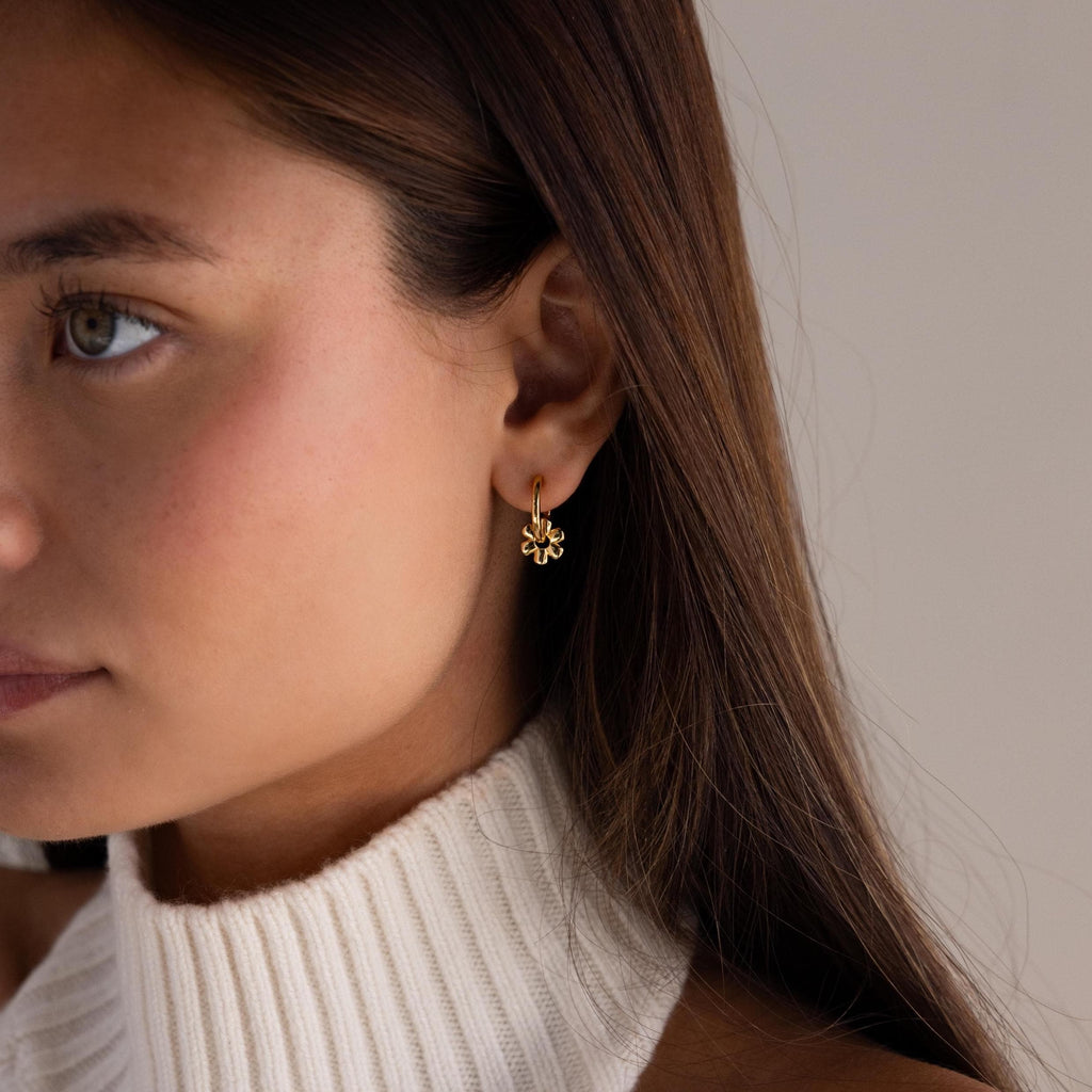 A woman wearing Dangling Blossom Huggies and a white knit turtleneck sweater.