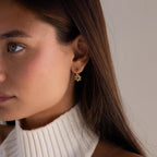 A woman wearing Dangling Blossom Huggies and a white knit turtleneck sweater.