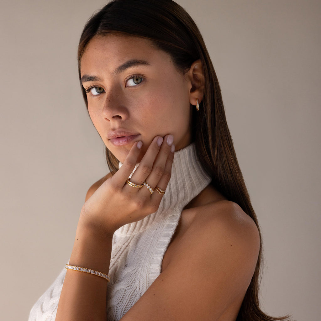 Woman with long brown hair wears a sleeveless knit top and touches her face thoughtfully, showcasing Baguette Birthstone Link Earrings.