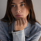 A woman with long hair in a denim jacket wears the Dainty Round Moonstone Ring, gazing thoughtfully into the distance.