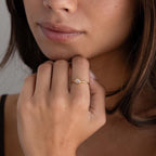 A woman gently touches her chin while wearing the Dainty Round Moonstone Ring, featuring a luminous white stone—an elegant and grounding jewelry piece.