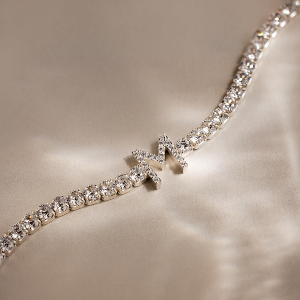Diamond Tennis Initial Bracelet with a chic M charm, shown on a silky beige background. Stackable and perfect for choosing your own initial for a personalized style.