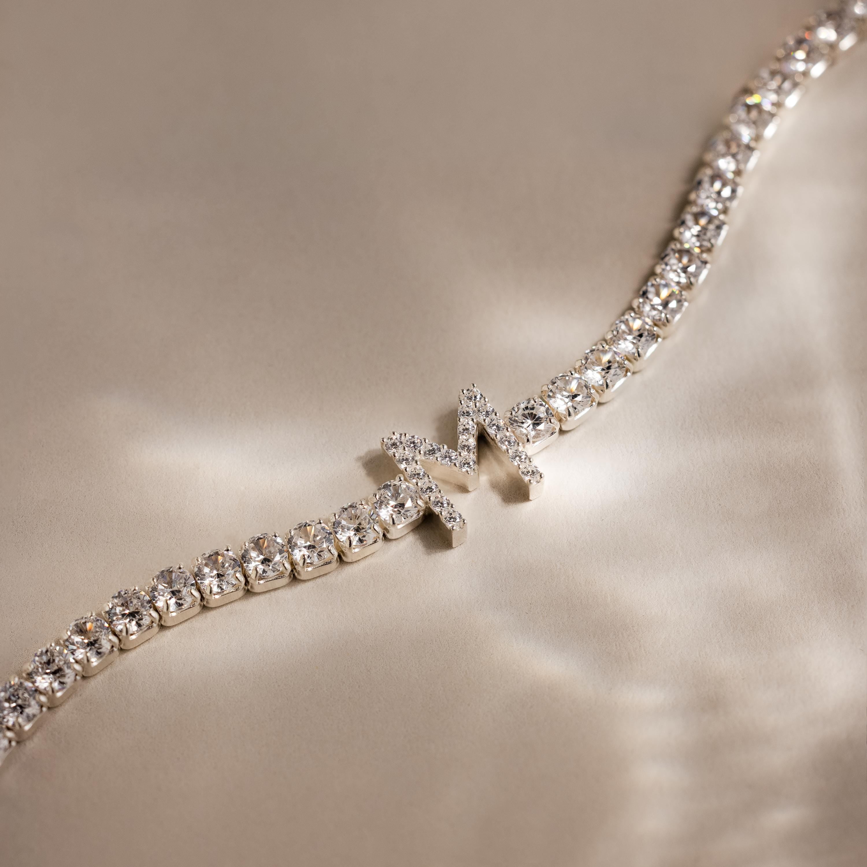 Diamond Tennis Initial Bracelet with a chic M charm, shown on a silky beige background. Stackable and perfect for choosing your own initial for a personalized style.