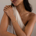 Woman in a white, one-shoulder top wears our Diamond Birthstone Tennis Bracelet, with arms gently crossed.