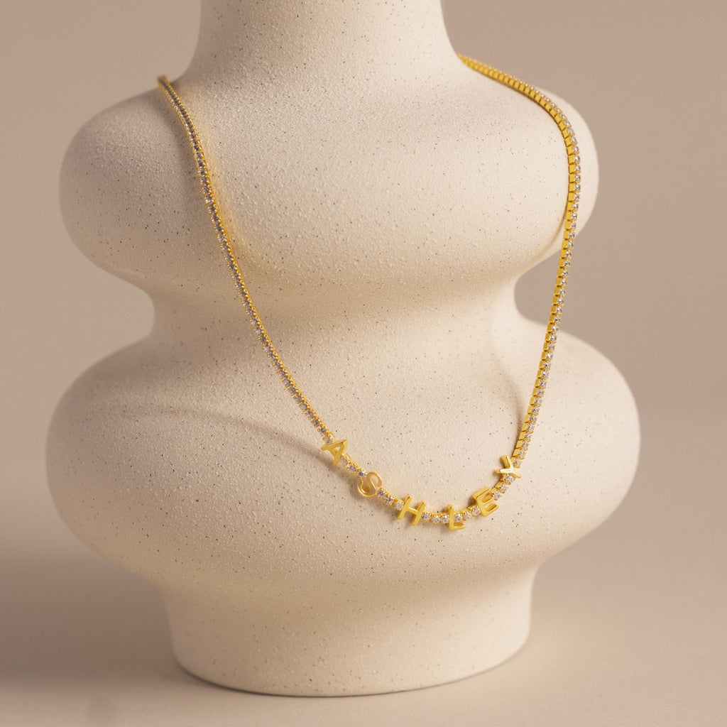 The Diamond Tennis Letter Necklace, spelling “Mother,” is elegantly displayed on a curvy, light beige ceramic bust—an ideal, sparkling tribute to celebrate mom in timeless style.