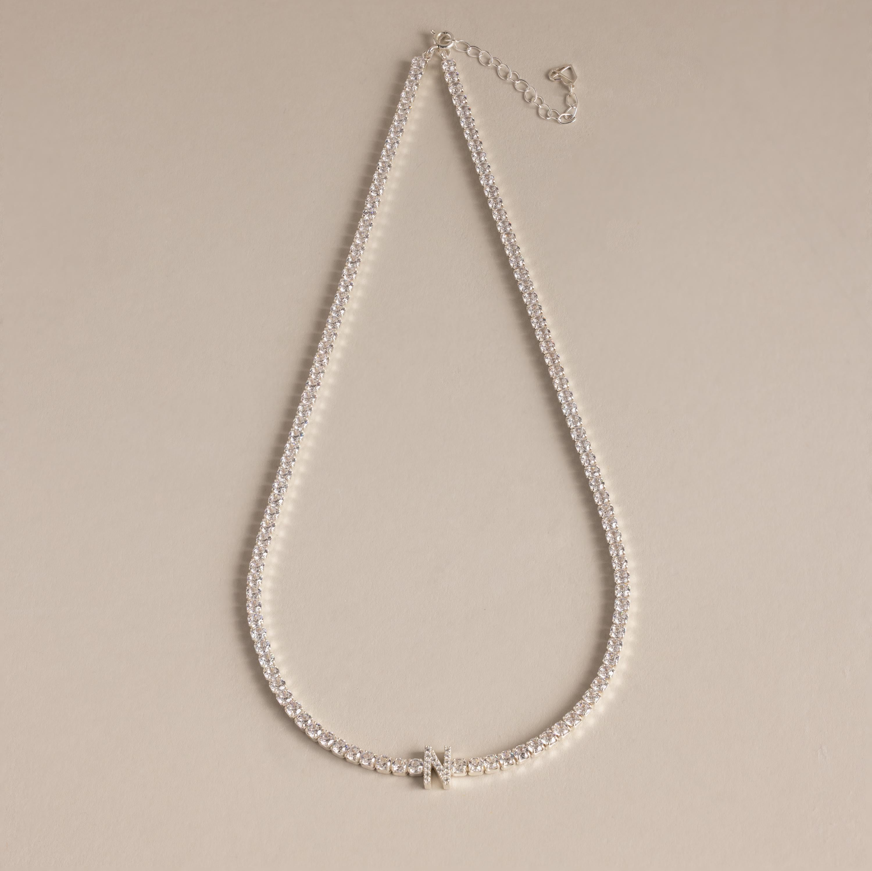 Diamond Tennis Initial Necklace featuring a sparkling initial pendant, ideal for layering with other personalized jewelry, showcased on a beige background.