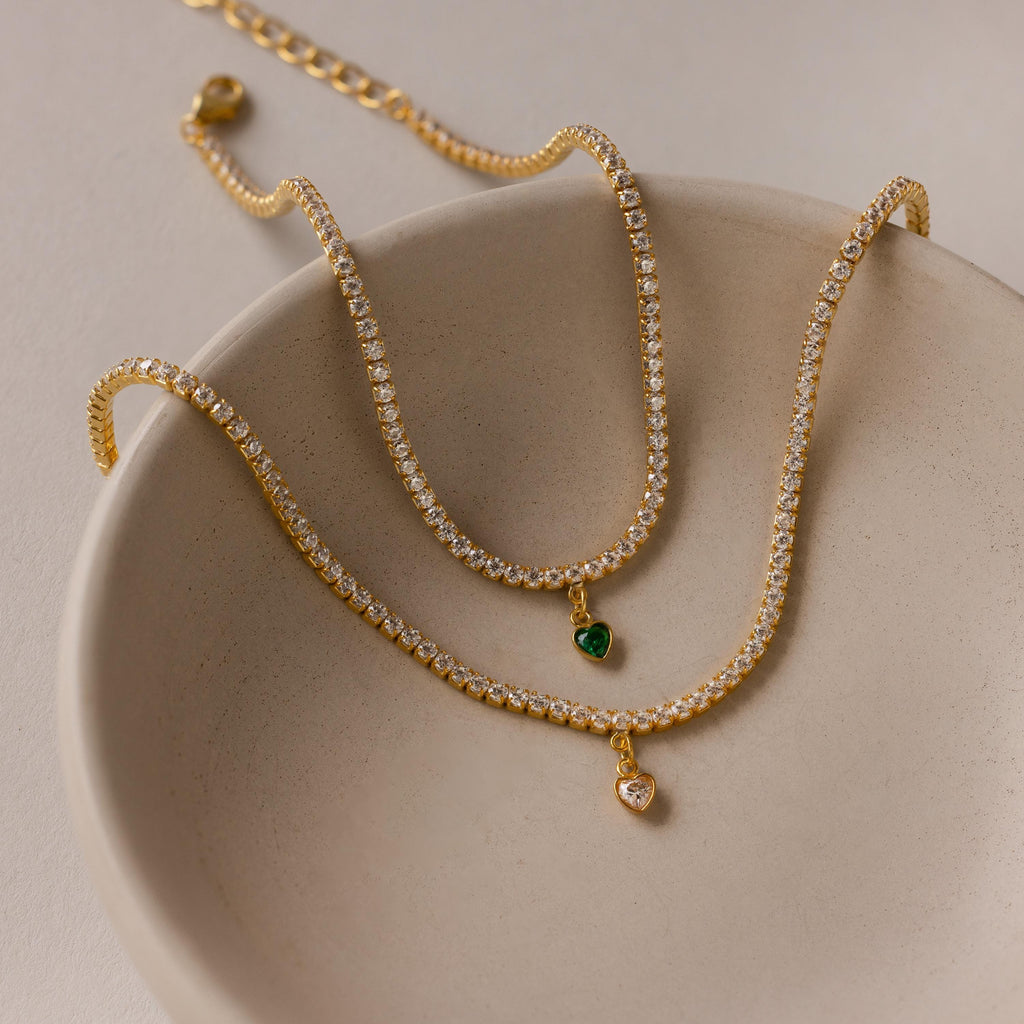 A Heart Birthstone Tennis Bracelet with a personalized heart-shaped charm, accented by sparkling CZ birthstones, elegantly displayed in a beige dish.