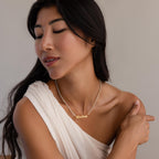 A woman in a white off-shoulder top looks down and gently touches her shoulder while wearing the Diamond Tennis Name Necklace personalized with "Lindsay.