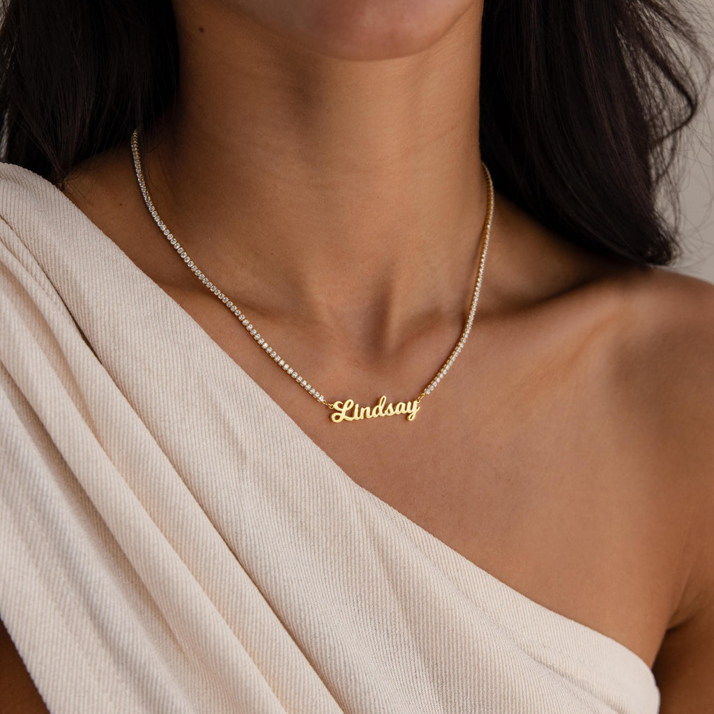 A woman wearing a Diamond Tennis Name Necklace with "Lindsay" and a cream off-shoulder top.