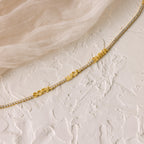 The Multiple Name Tennis Bracelet featuring SOFIA, LUCA, and EMMA rests on a textured white surface with beige fabric—an elegant way to display stylish custom name charms.