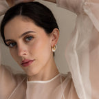 A woman with dark hair models Bold Round Pearl Hoops, making a statement with these elegant, eye-catching earrings and a sheer light blouse.
