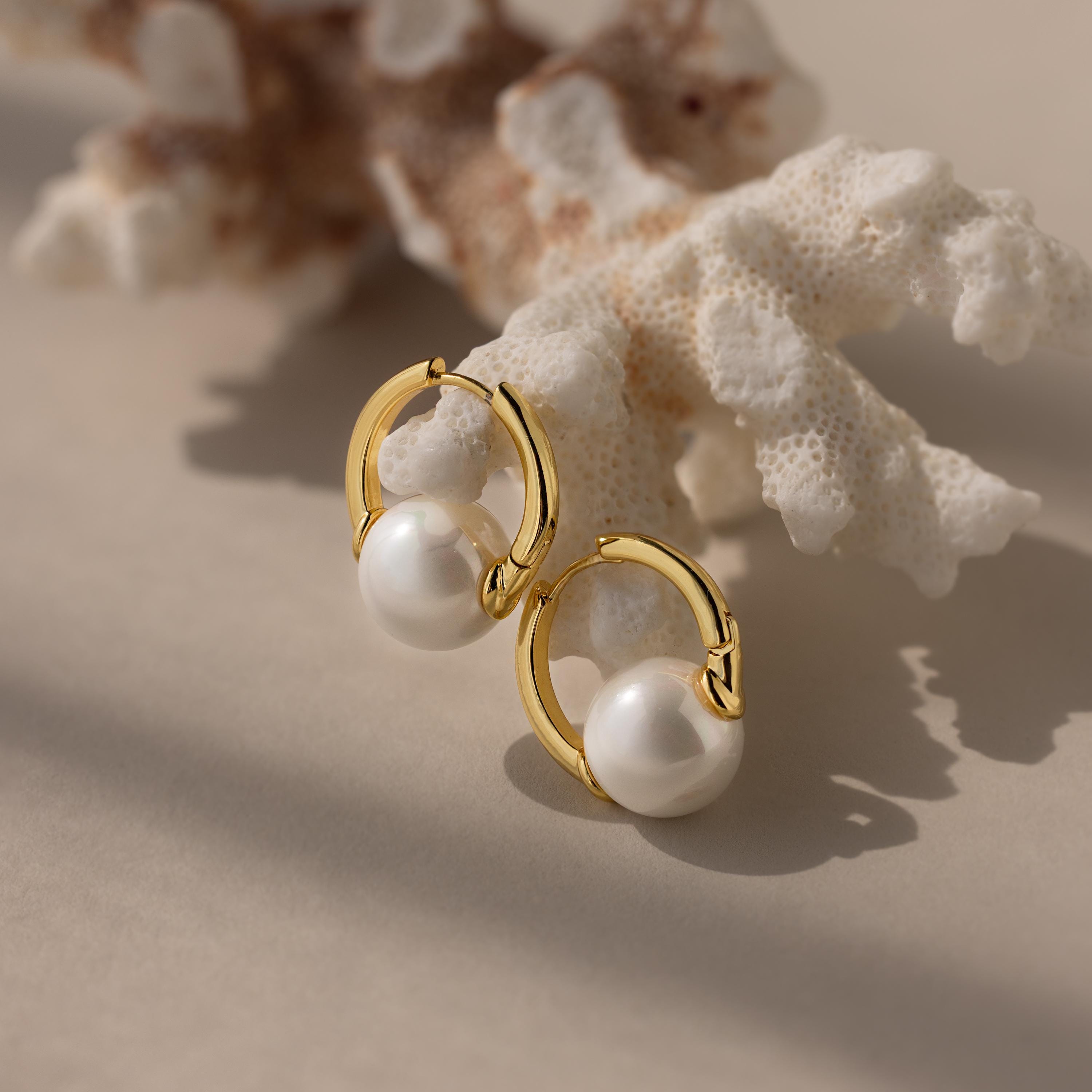 Bold Round Pearl Hoops feature gold accents and pearls, elegantly displayed on coral—perfect statement earrings for any occasion.
