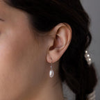 A close-up of a woman's ear wearing Dangling Pearl Diamond Earrings, her dark hair pulled back to showcase the elegant jewelry.
