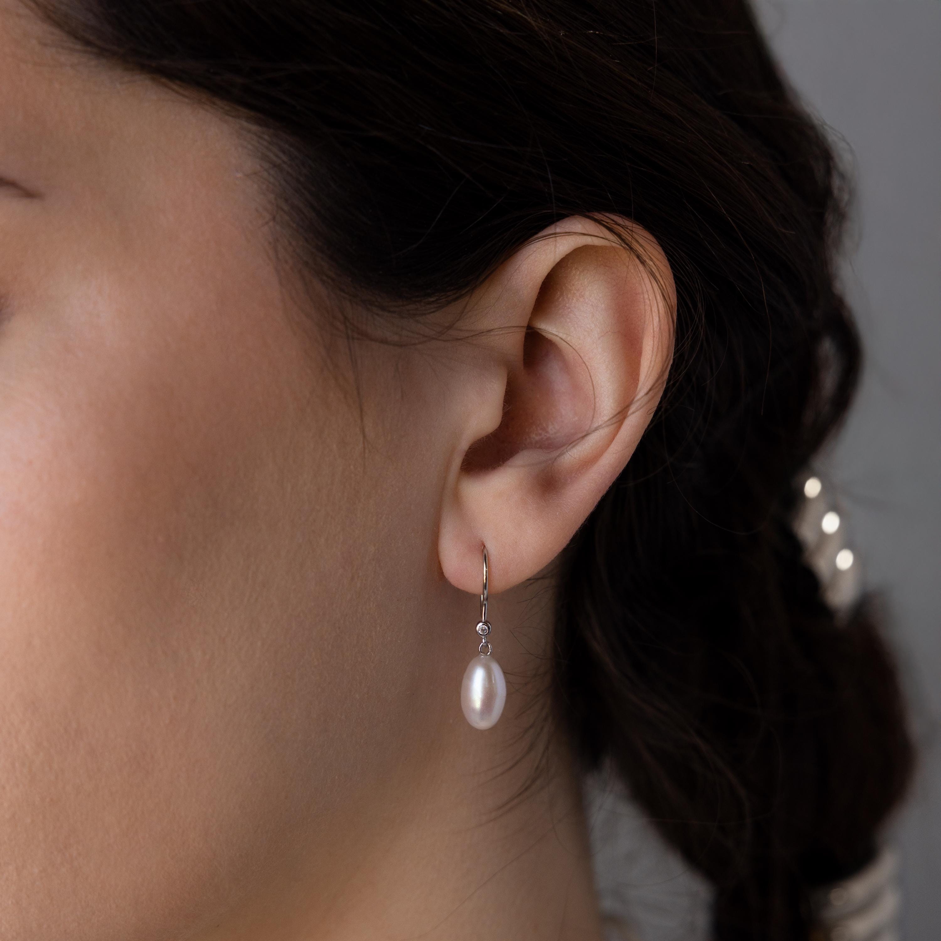 A close-up of a woman's ear wearing Dangling Pearl Diamond Earrings, her dark hair pulled back to showcase the elegant jewelry.