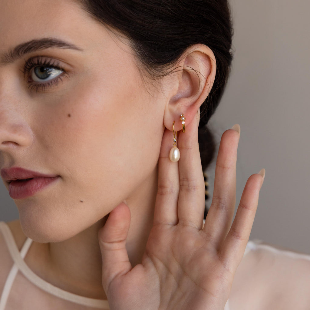 A woman with fair skin showcases the elegant Dangling Pearl Diamond Earrings—gold hoops adorned with pearls gently touching her ear.