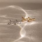 Four Dainty Pearl Bar Studs, featuring two silver and two gold designs, are displayed on a softly lit neutral surface.
