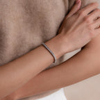 A person wearing the S-Link Diamond Tennis Bracelet, featuring shimmering stones on their wrist, styled with a beige top.