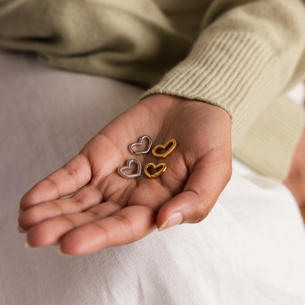 A hand displays the Heart Carabiner Set in Sterling Silver, featuring two gold and two silver heart-shaped jewelry rings—ideal as charm bracelet connectors—against a neutral background.