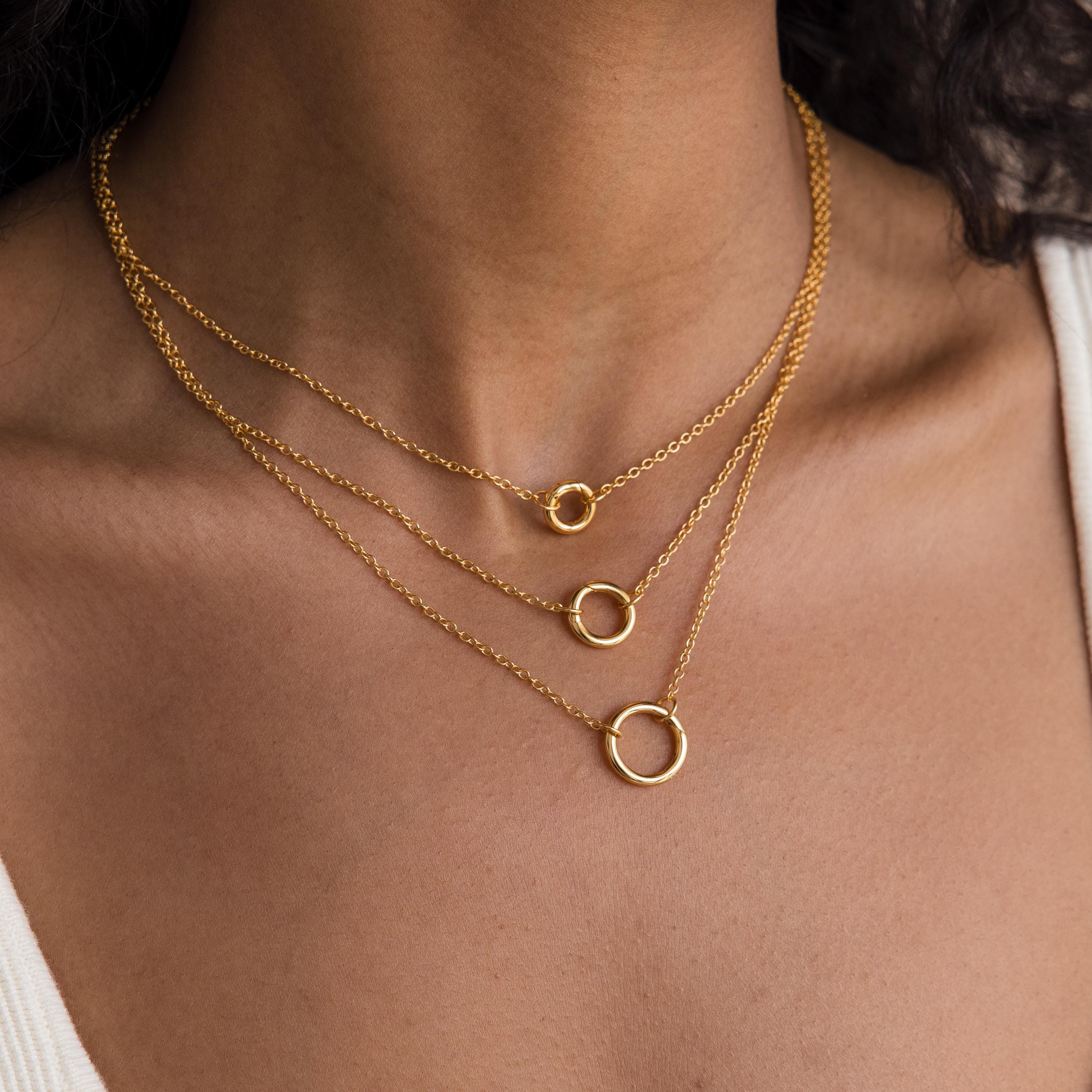 A woman wears the Round Carabiner Charm Set in 18K Gold, featuring three gold chain necklaces with small, medium, and large circle pendants styled as a charm necklace.
