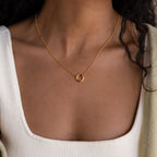 A woman wears the Cable Circle Charm Necklace with a white square-neck top and a beige sweater.