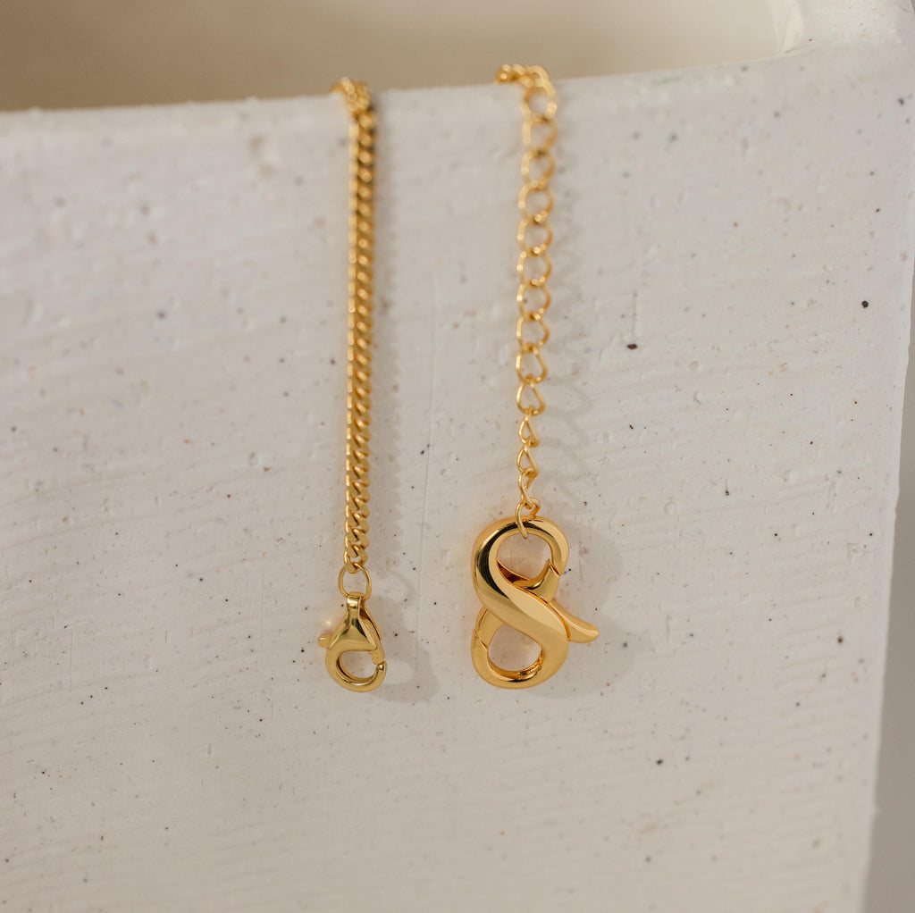 Two 18K gold necklaces from the Multipurpose Lobster Clasp Extender Set, each with a letter A or S pendant, are displayed on a white textured surface. Both feature an adjustable lobster clasp for versatile styling.