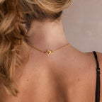 Close-up of a woman's neck with wavy blond hair in a ponytail, showcasing the Multipurpose Lobster Clasp Extender Set in 18K Gold attached to the back of her gold necklace.