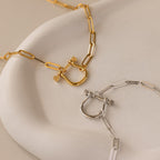 The Bar & Carabiner Charm Set in 18K Gold is elegantly displayed on a white ceramic dish.