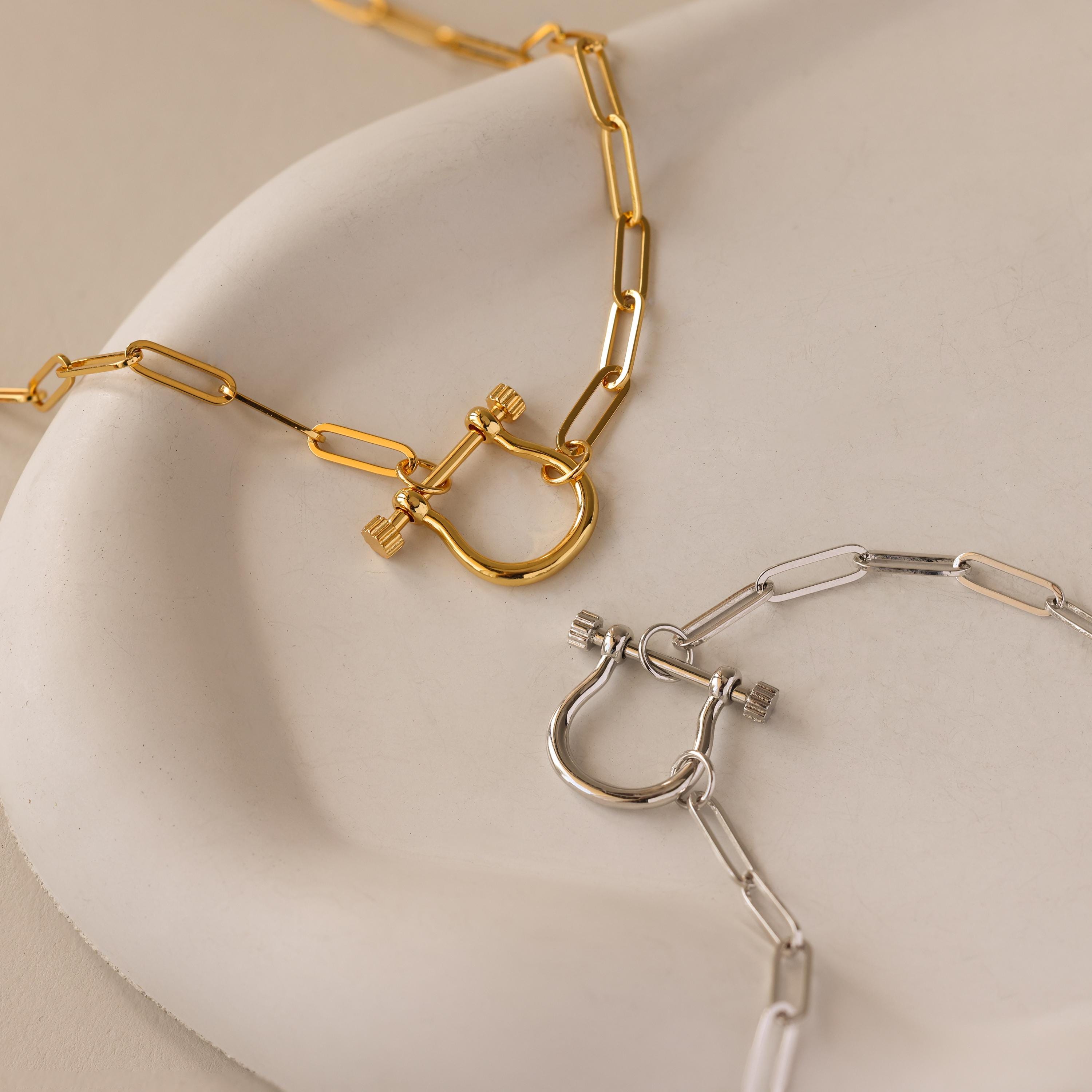 The Bar & Carabiner Charm Set in 18K Gold is elegantly displayed on a white ceramic dish.