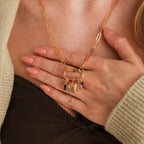 Close-up of a woman's hands on her chest, highlighting the Bar & Carabiner Charm Set in 18K Gold, featuring necklace charms and a heart pendant secured by a sleek carabiner connector.