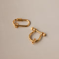 Two gold charm connectors—one oval and one U-shaped with a bar—rest on a smooth beige surface, perfect as necklace accessories or as part of the Bar & Carabiner Charm Set.