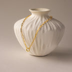 Paperclip Clasp Necklace draped over a textured white ceramic vase on a neutral background, featuring collectible charms for a unique touch.