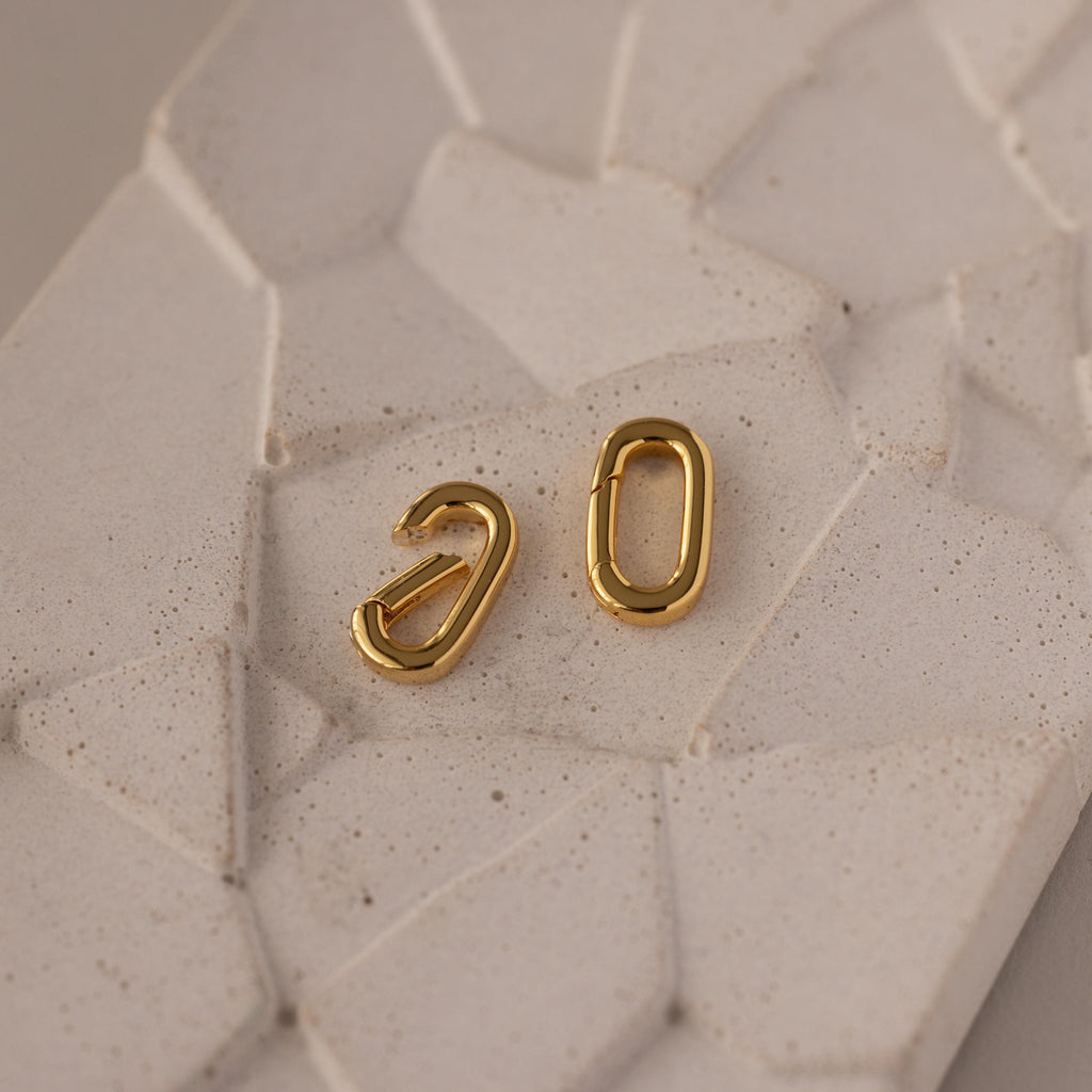 The Multipurpose Charm Hoop Clasp Set in White Gold features two oval charms on a light, textured surface—perfect for stacking bracelets or as a stylish charm connector.