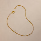 The Diamond Tennis Clasp Necklace features small, evenly spaced diamonds and a secure rolo clasp, laid in an S-shape on a light beige background—a stunning choice for wedding jewelry.