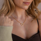 A woman shown from the shoulders up wears the Rolo Heart Clasp Necklace featuring a heart-shaped clasp, paired with a brown top and beige sweater.